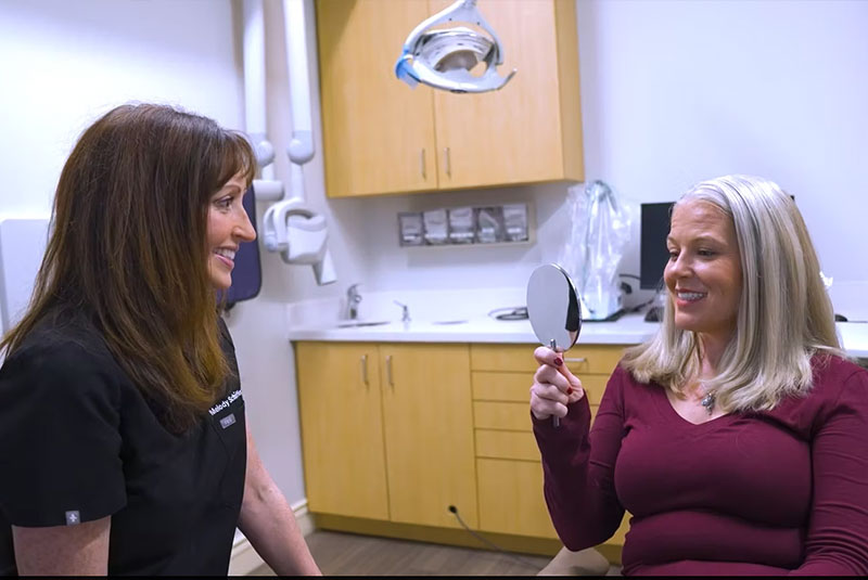 Dr.Melody Schiffer giving mirror to patient so they can their teeth after dental procedure